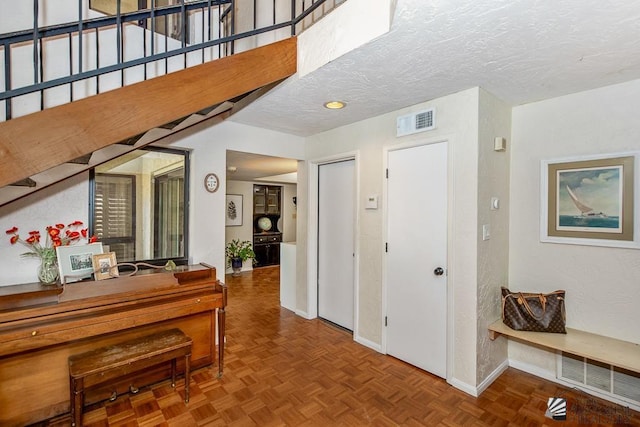corridor featuring visible vents, a textured ceiling, baseboards, and stairs