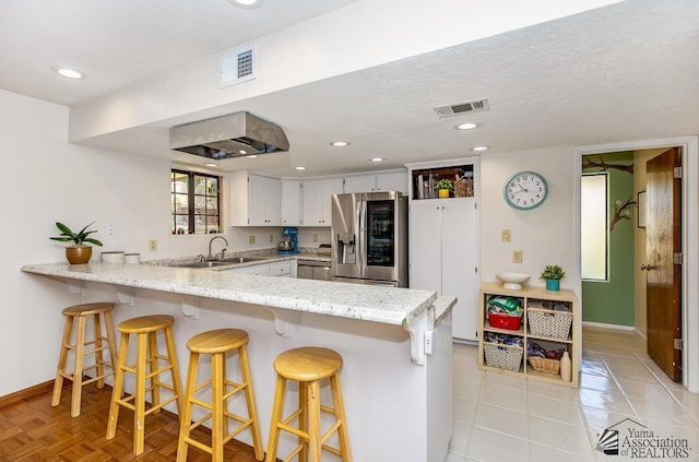 kitchen with a sink, a peninsula, baseboards, stainless steel refrigerator with ice dispenser, and visible vents