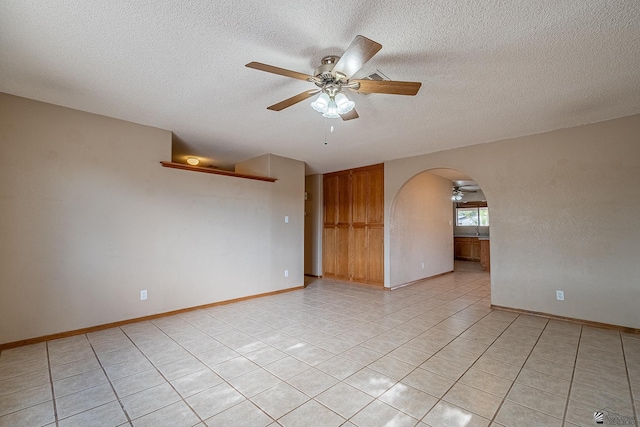spare room with light tile patterned floors, arched walkways, a ceiling fan, and a textured ceiling