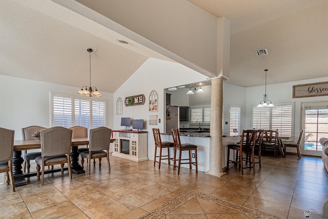 dining space featuring a chandelier, high vaulted ceiling, a textured ceiling, and ornate columns