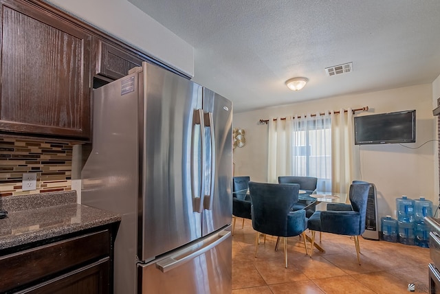kitchen featuring light tile patterned flooring, dark brown cabinetry, freestanding refrigerator, backsplash, and visible vents