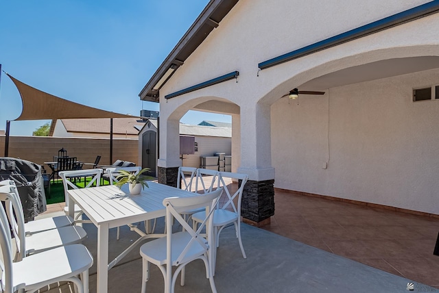 view of patio featuring ceiling fan, fence, an outdoor structure, a shed, and outdoor dining space