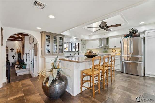 1925 S Ridgeview Dr, Yuma, AZ 85364 - kitchen featuring wall chimney range hood, visible vents, arched walkways, freestanding refrigerator, and glass insert cabinets