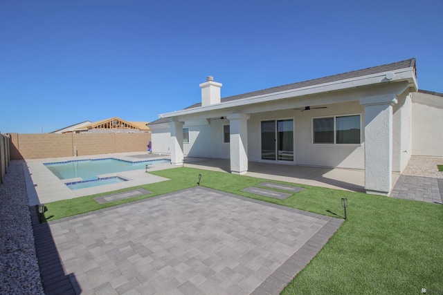 rear view of house with ceiling fan, stucco siding, a fenced backyard, an in ground hot tub, and a patio area