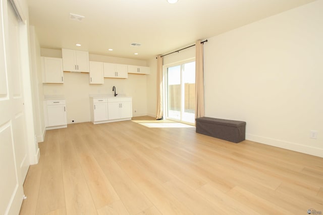 unfurnished living room with recessed lighting, baseboards, light wood finished floors, and a sink