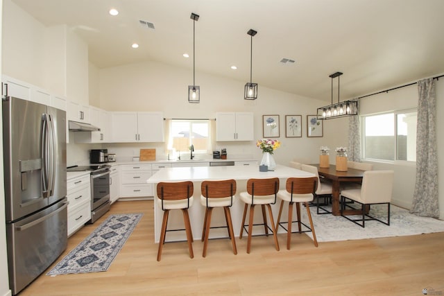 kitchen featuring a healthy amount of sunlight, a kitchen bar, under cabinet range hood, a sink, and appliances with stainless steel finishes