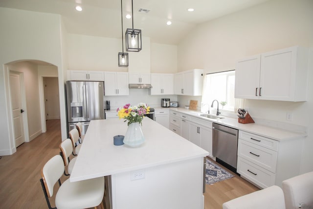 kitchen featuring a breakfast bar, high vaulted ceiling, arched walkways, a sink, and appliances with stainless steel finishes