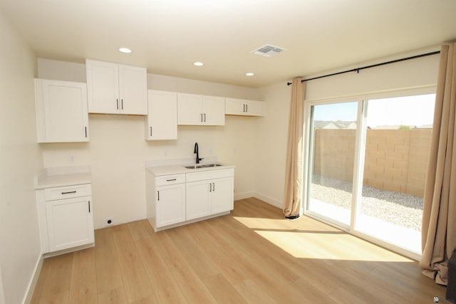 kitchen featuring visible vents, recessed lighting, white cabinets, a sink, and light wood-style flooring