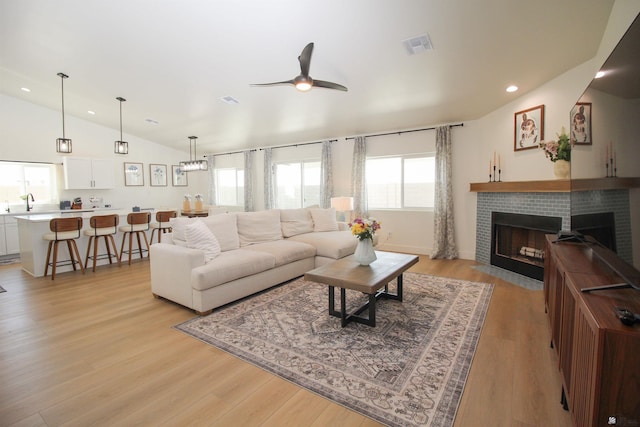 living area with light wood-style floors, a brick fireplace, a ceiling fan, lofted ceiling, and visible vents
