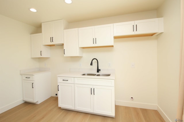 kitchen featuring light wood-style floors, a sink, white cabinetry, and baseboards