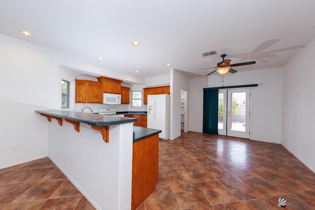 kitchen with visible vents, brown cabinetry, a peninsula, dark countertops, and white appliances