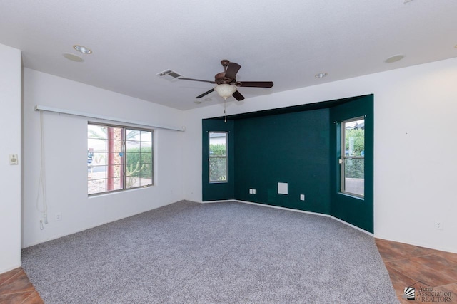 spare room featuring carpet floors, a ceiling fan, visible vents, and a healthy amount of sunlight