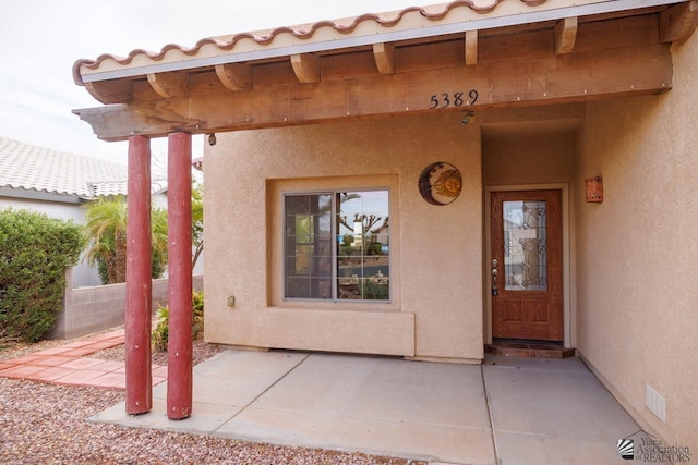 view of exterior entry featuring a patio area, stucco siding, and a tile roof