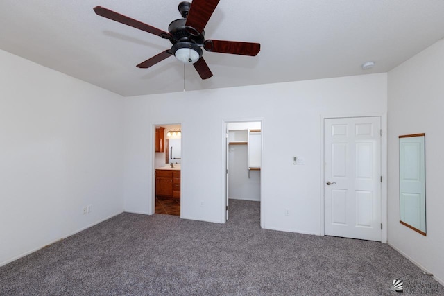 unfurnished bedroom featuring ceiling fan, a closet, dark colored carpet, a spacious closet, and ensuite bathroom