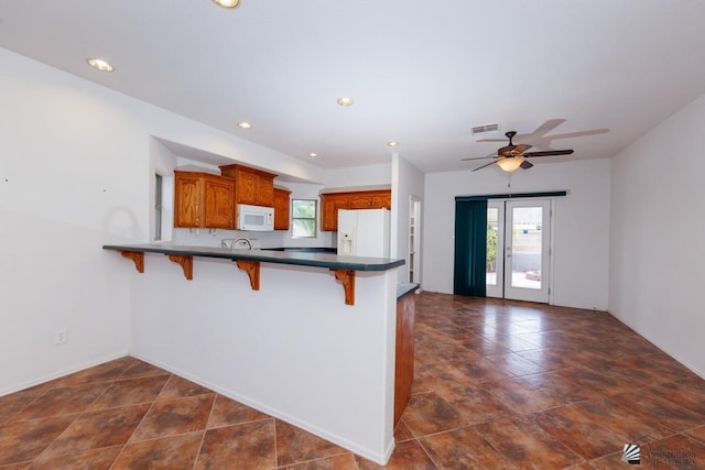 kitchen with a breakfast bar area, visible vents, brown cabinets, a peninsula, and white appliances
