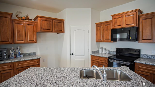 kitchen with a sink, light stone countertops, black appliances, and brown cabinetry