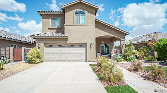 mediterranean / spanish-style house with fence, a tile roof, concrete driveway, stucco siding, and a garage