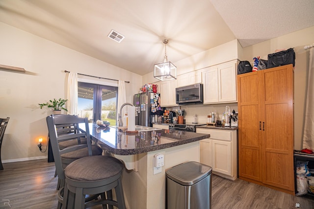 kitchen featuring visible vents, a breakfast bar, a sink, dark wood finished floors, and stainless steel appliances