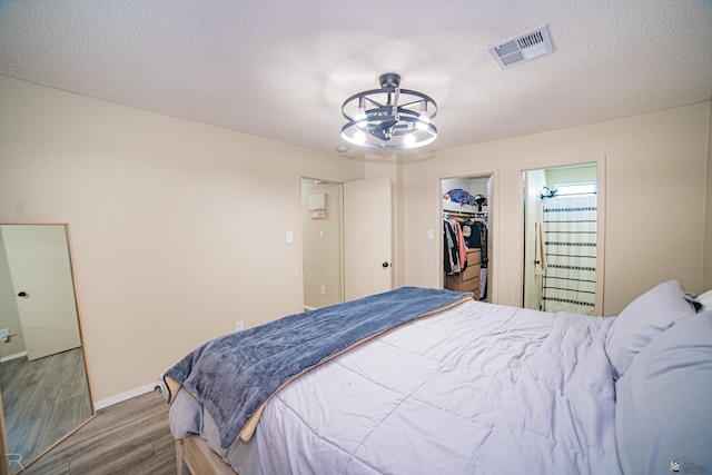 bedroom with a walk in closet, visible vents, wood finished floors, baseboards, and a notable chandelier