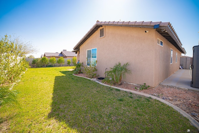 view of side of property with a yard, a tiled roof, fence, and stucco siding