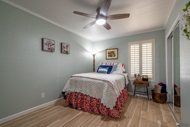 bedroom with a ceiling fan, wood finished floors, baseboards, a closet, and ornamental molding