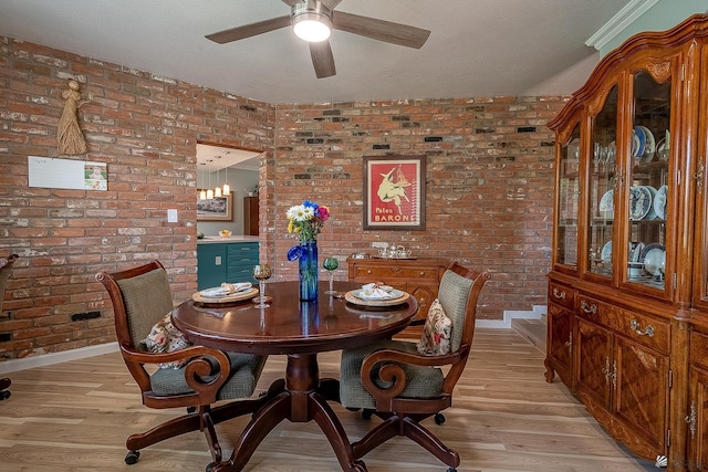 dining room with light wood-type flooring, ceiling fan, and brick wall