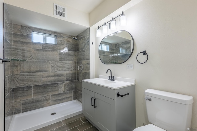 full bathroom with visible vents, vanity, toilet, and tiled shower