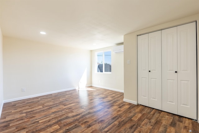 unfurnished bedroom featuring a closet, baseboards, a wall mounted air conditioner, recessed lighting, and dark wood finished floors