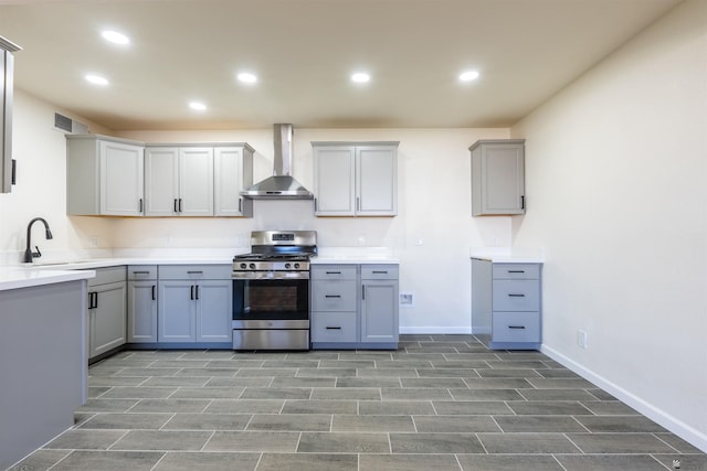 kitchen featuring wall chimney range hood, gray cabinets, stainless steel range with gas stovetop, a sink, and recessed lighting