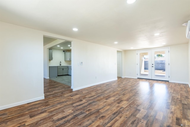 unfurnished living room with french doors, dark wood finished floors, baseboards, an AC wall unit, and recessed lighting