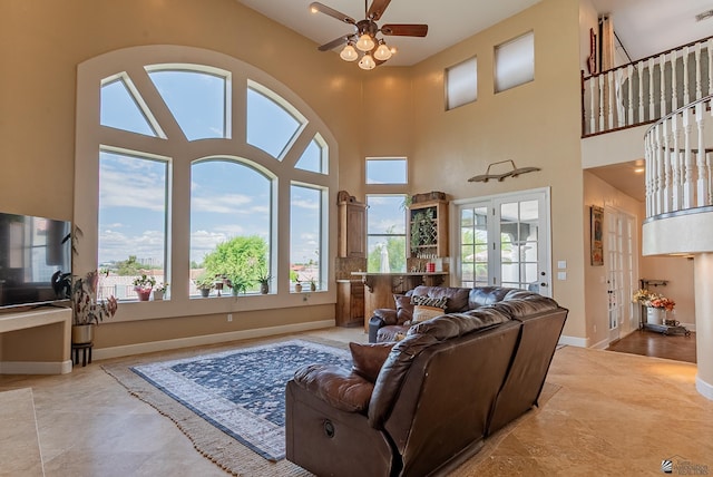 living room featuring healthy amount of natural light, a ceiling fan, baseboards, and a towering ceiling