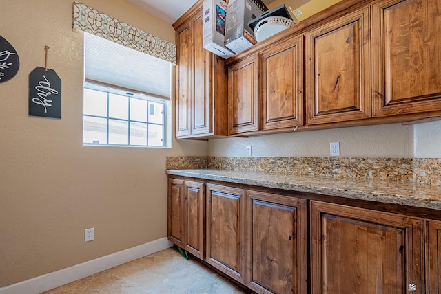 kitchen featuring brown cabinets, baseboards, and light stone countertops