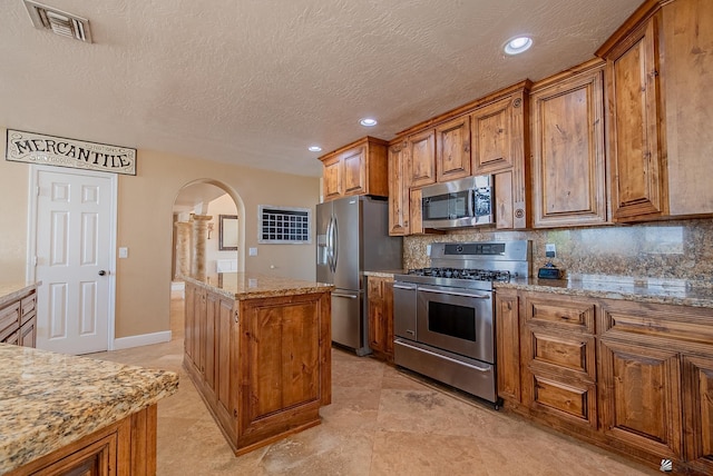 kitchen featuring appliances with stainless steel finishes, arched walkways, brown cabinets, a center island, and recessed lighting