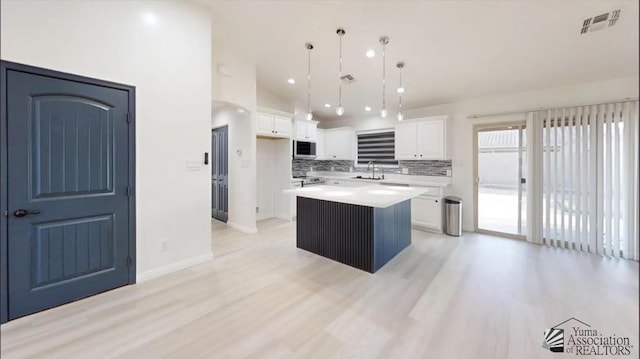 kitchen featuring pendant lighting, a kitchen island, white cabinets, and backsplash