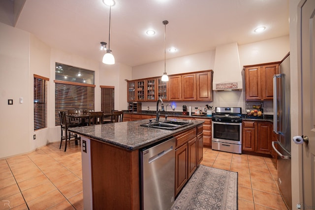 kitchen with light tile patterned flooring, appliances with stainless steel finishes, a sink, brown cabinetry, and premium range hood