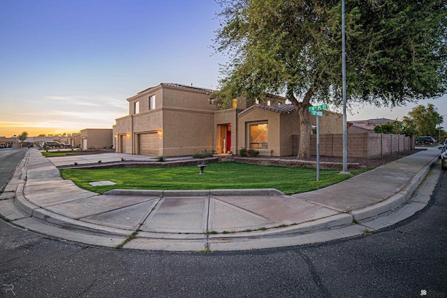 view of front facade with a yard, fence, concrete driveway, an attached garage, and stucco siding