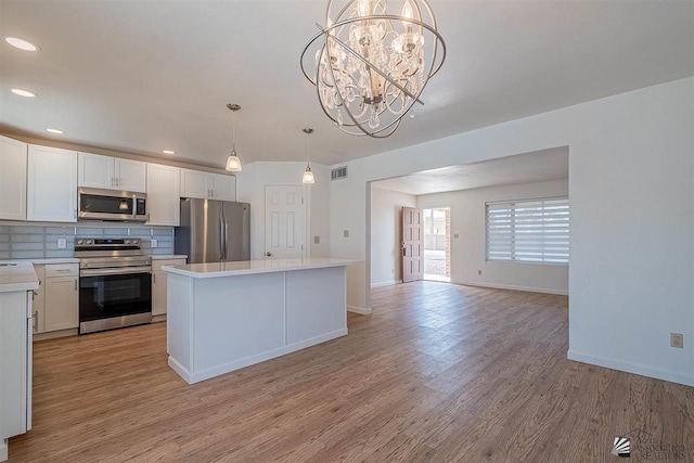 kitchen with appliances with stainless steel finishes, pendant lighting, white cabinetry, and a kitchen island