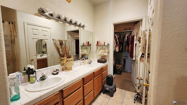 full bath with a sink, tile patterned flooring, double vanity, and a spacious closet