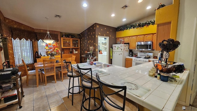 kitchen with a sink, white appliances, tile counters, wallpapered walls, and visible vents