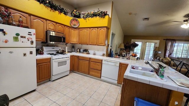 kitchen with visible vents, a peninsula, white appliances, tile countertops, and a sink