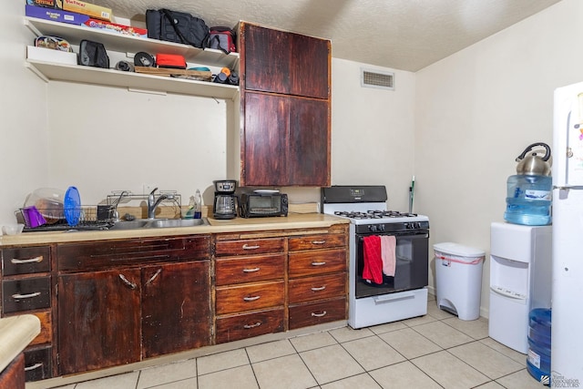 1127 S 13th Ave, Yuma, AZ 85364 - kitchen featuring gas stove, light countertops, light tile patterned flooring, open shelves, and reddish brown cabinets
