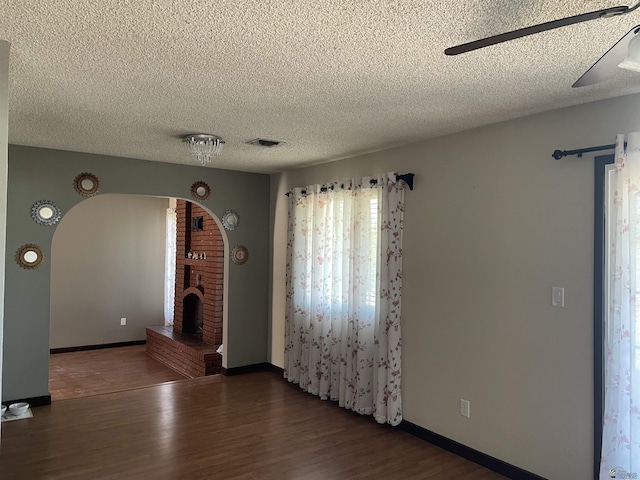 1603 S 31st Dr, Yuma, AZ 85364 - unfurnished room featuring arched walkways, wood finished floors, a textured ceiling, and a brick fireplace