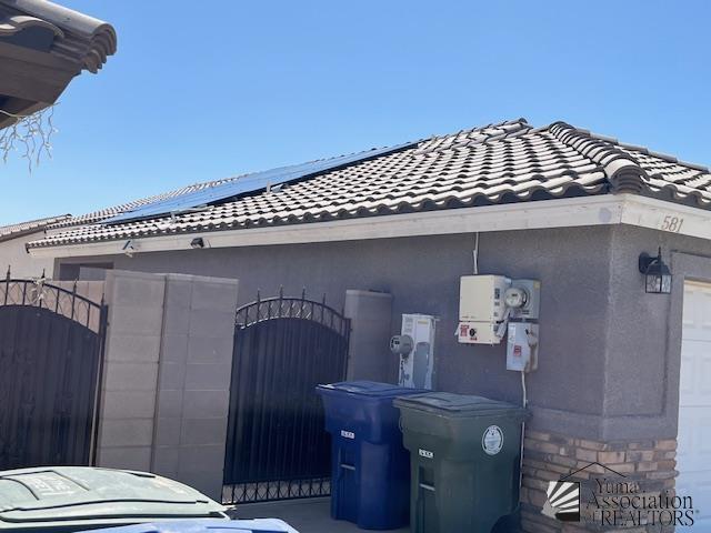 view of side of property with a gate, stucco siding, a tiled roof, and stone siding