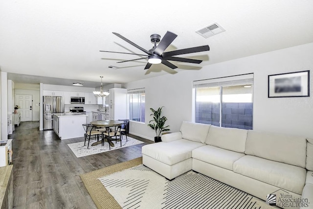 living room featuring visible vents, dark wood finished floors, ceiling fan with notable chandelier, and baseboards