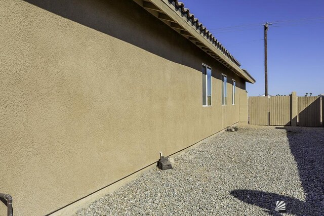 view of side of property featuring fence, a tile roof, and stucco siding