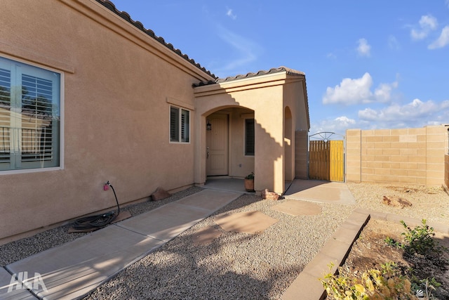 property entrance featuring a gate, stucco siding, a tile roof, and fence