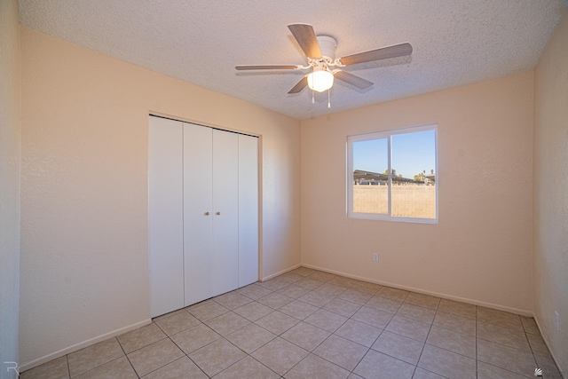 unfurnished bedroom featuring ceiling fan, light tile patterned flooring, a textured ceiling, and a closet