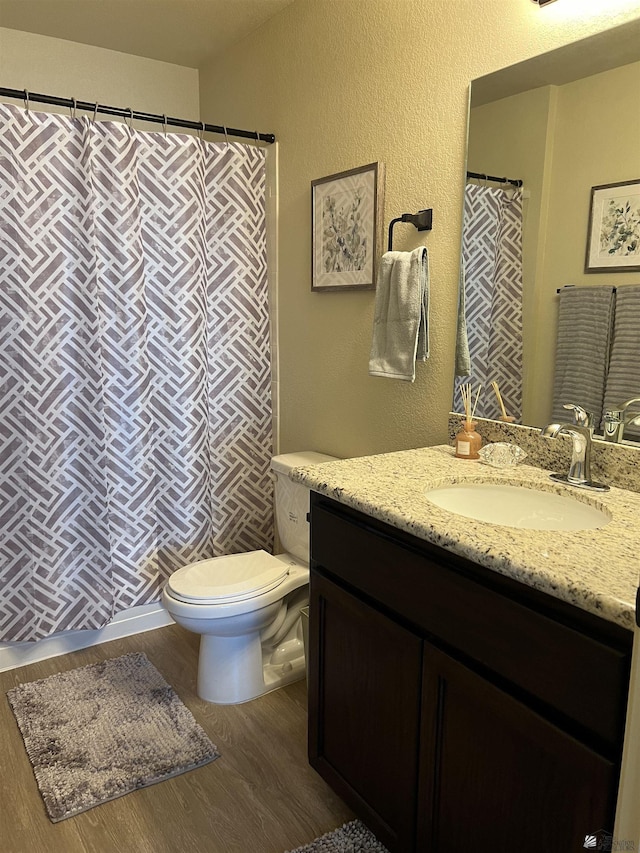 full bath with vanity, a textured wall, wood finished floors, and toilet