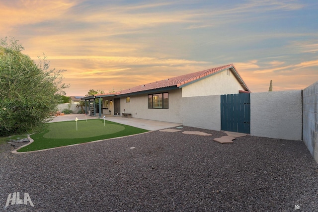 back of property at dusk featuring a fenced backyard, a patio, stucco siding, and a tiled roof