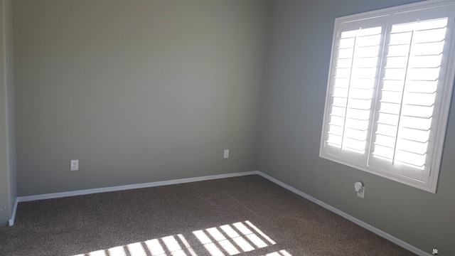 spare room featuring dark carpet and baseboards